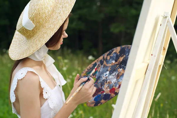 Красивая женщина в шляпе художник рисует картину на природе — стоковое фото