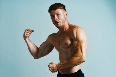 Kaslı vücutlu vücut geliştirici mavi arka plana basar