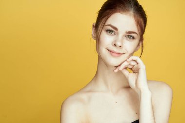 Çıplak omuzlu, beyaz tenli, sarı arkaplan pozu veren bir kadın.