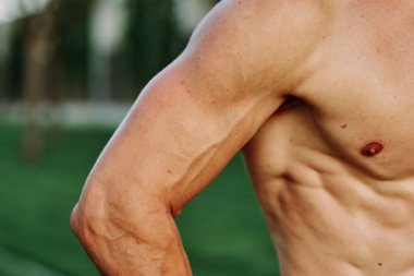 Şişirilmiş kaslı vücutlu bir adam dışarıda sağlık egzersizi yapıyor.