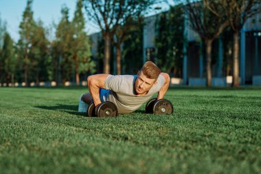 Atletik adam sabah halterlerle antrenman yapıyor. Park.