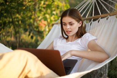 Kadınlar dışarıda bir hamakta dizüstü bilgisayarlı internetle yatıyor.