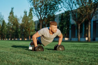 Atletik adam sabah halterlerle antrenman yapıyor. Park.