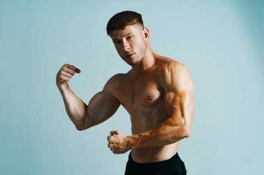 Kaslı vücutlu vücut geliştirici mavi arka plana basar