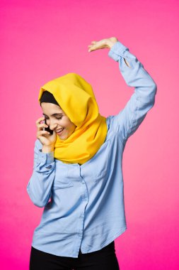 Sarı tesettürlü müslüman kadın telefon teknolojisi pembe arka planda konuşuyor.