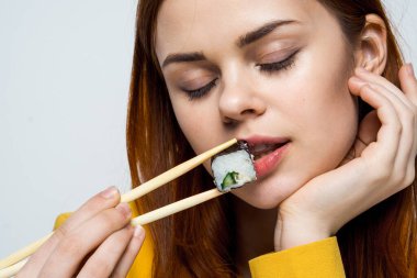 Japon yemek çubuklarıyla suşi yiyen kadın arka planda ışık yayıyor.