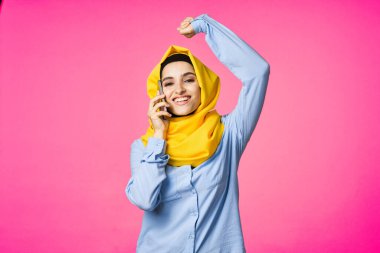 Sarı tesettürlü müslüman kadın telefon teknolojisi pembe arka planda konuşuyor.