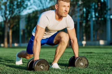 Atletik adam sabah halterlerle antrenman yapıyor. Park.