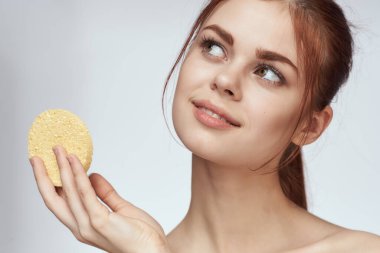 Ellerinde süngerle çıplak omuzlarıyla cilt bakımı yapan bir kadın.