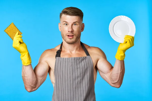 Muž v zástěře čištění nádobí mytí modré pozadí — Stock fotografie