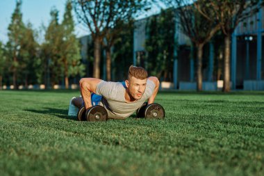 Atletik adam sabah halterlerle antrenman yapıyor. Park.