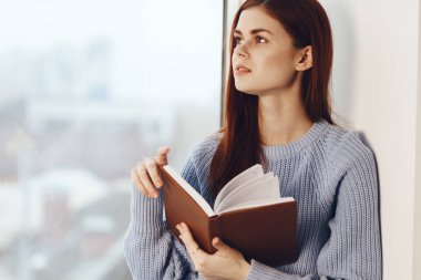 Kadın pencerenin yanında kitap okuyor, bir bardak içkiyle dinleniyor.