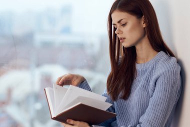 Kadın pencerenin yanında kitap okuyor, bir bardak içkiyle dinleniyor.