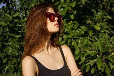 Yeşil yaprakların arkasında poz veren çekici bir kadın.