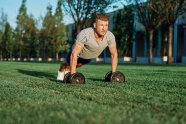 Atletik adam sabah halterlerle antrenman yapıyor. Park.