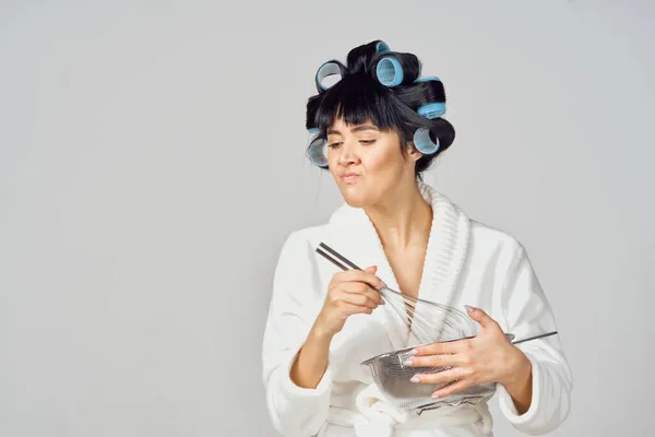 Женщина в белом халате с бигудями на голове делает домашнее задание на кухне — стоковое фото