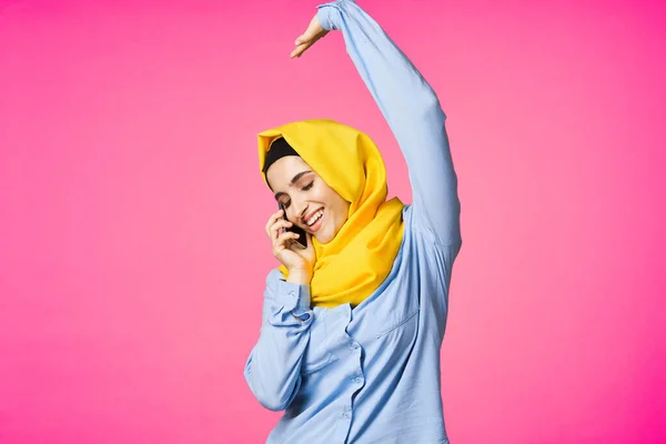 Muslim kvinna i gul hijab talar på telefonen teknik rosa bakgrund — Stockfoto