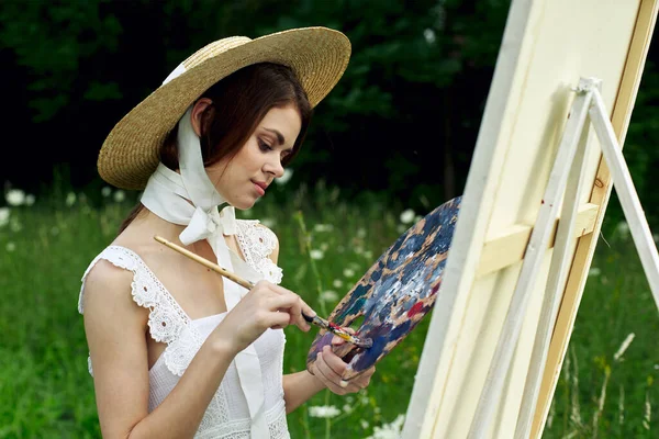 Mooie vrouw in hoed kunstenaar schildert een beeld op de natuur verf — Stockfoto