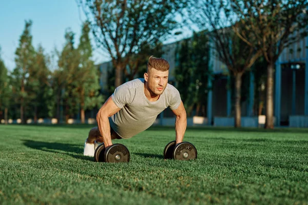 Atletik adam sabah halterlerle antrenman yapıyor. Park.
