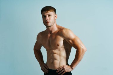 Kaslı vücutlu vücut geliştirici mavi arka plana basar