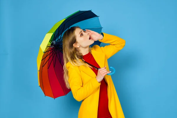 身穿黄色外套、头戴彩色雨伞、身披蓝色背景的女人 — 图库照片
