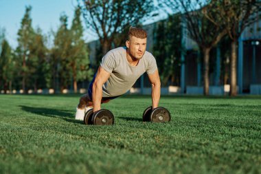 Atletik adam sabah halterlerle antrenman yapıyor. Park.