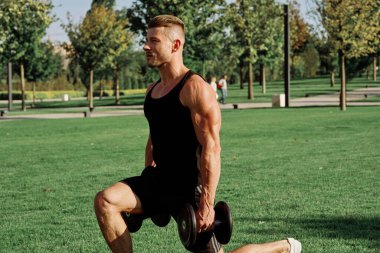 Siyah tişörtlü bir adam, doğa parkında dambıl egzersizi yapıyor.