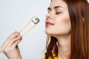 Japon yemek çubuklarıyla suşi yiyen kadın arka planda ışık yayıyor.