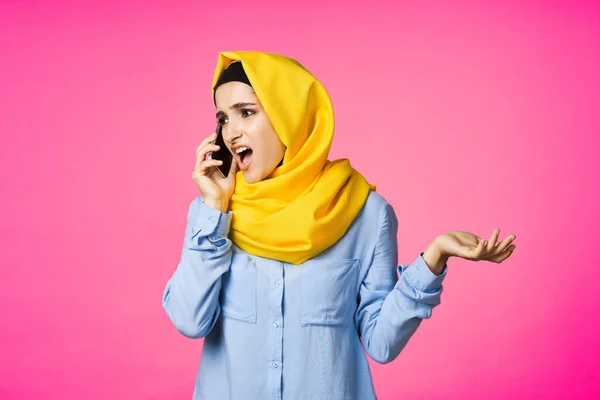 Мусульманська жінка в жовтому хіджабі говорить по телефону технології рожевий фон — стокове фото