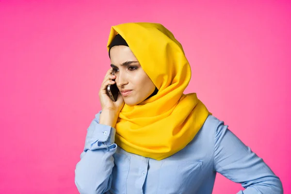 穿着黄色头巾的穆斯林妇女在电话粉色技术背景下交谈 — 图库照片