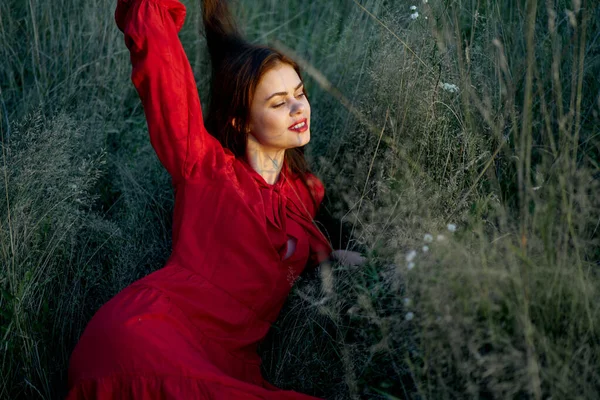 Όμορφη γυναίκα με κόκκινο φόρεμα βρίσκεται στο γρασίδι ήλιο της φύσης — Φωτογραφία Αρχείου