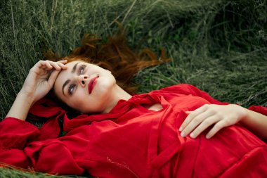Kırmızı elbiseli kadın yaz aylarında çim adreste yatıyor.