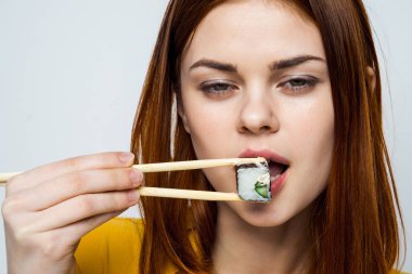 Japon yemek çubuklarıyla suşi yiyen kadın arka planda ışık yayıyor.