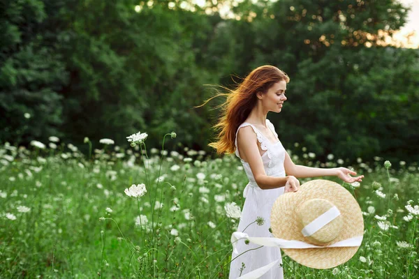Donna in abito bianco cappello che tiene fiori natura passeggiata — Foto Stock