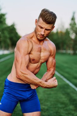 Şişirilmiş kaslı vücutlu bir adam dışarıda sağlık egzersizi yapıyor.
