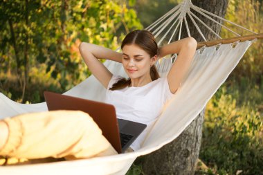 Kadınlar hamakta dizüstü bilgisayarlı tatil internetleriyle yatıyor.