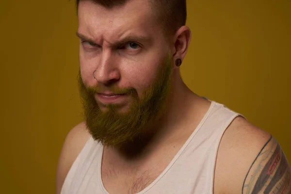 A bearded man with a serious expression in a white t-shirt with tattoos on his arms — Stock Photo, Image
