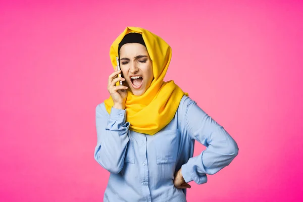 Donna musulmana in hijab giallo parlando sulla tecnologia del telefono sfondo rosa — Foto Stock