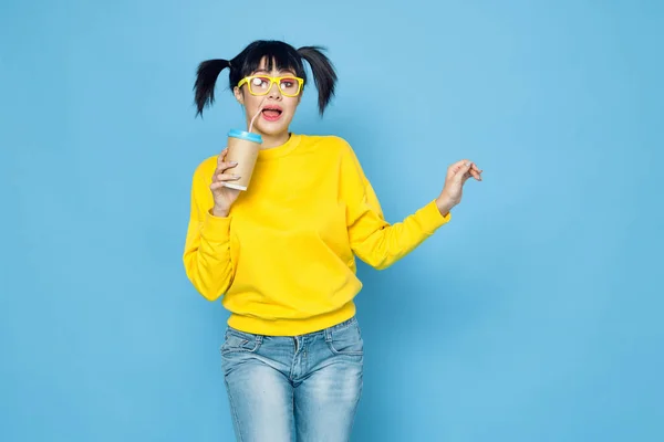 Fröhliche Frau mit Zöpfen im gelben Pullover trinken blauen Hintergrund — Stockfoto