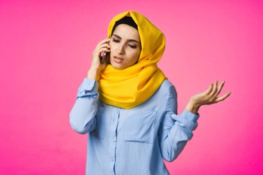 Sarı tesettürlü müslüman kadın telefonda pembe teknolojiyle konuşuyor.