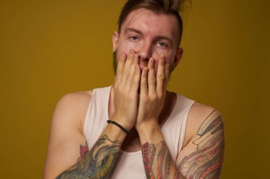 Beyaz tişörtlü, kollarında dövmeleri olan sakallı bir adam.