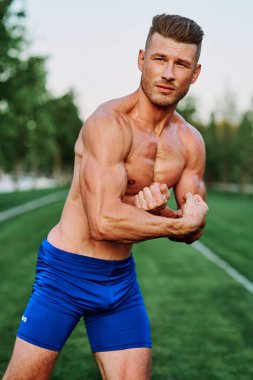 Şişirilmiş kaslı vücutlu bir adam dışarıda sağlık egzersizi yapıyor.