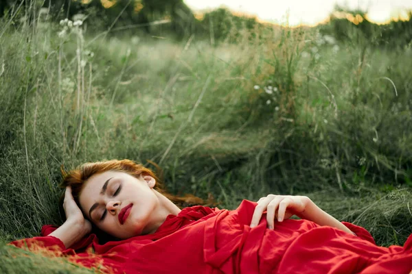 Hübsche Frau im roten Kleid liegt auf dem Gras — Stockfoto