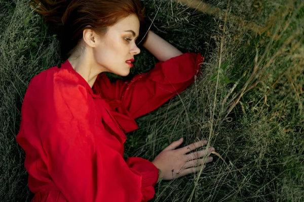 Pretty woman in red dress lies on the grass sun summer nature — Stock Photo, Image