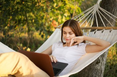 Kadınlar dışarıda bir hamakta dizüstü bilgisayarlı internetle yatıyor.
