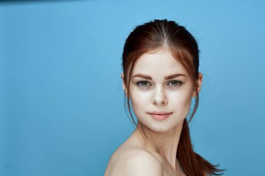 Çıplak omuzlu, at kuyruklu, mavi arka plan pozu veren bir kadın.