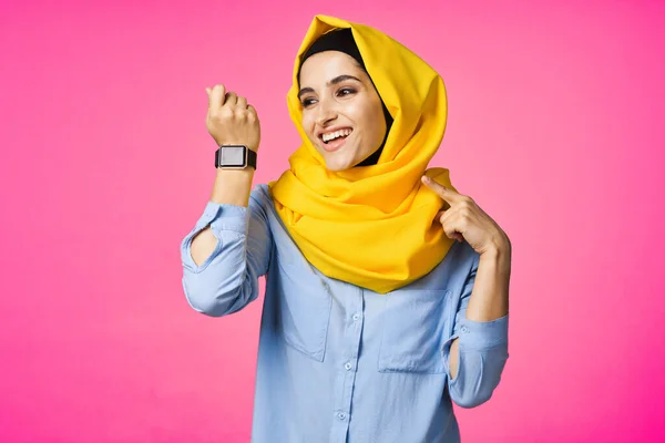 Mujer alegre en amarillo hijab reloj electrónico tecnología usuario rosa fondo —  Fotos de Stock