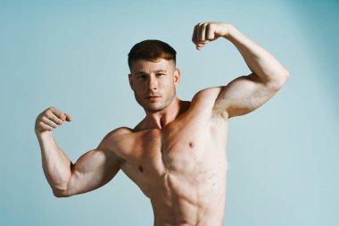 Kaslı vücutlu vücut geliştirici mavi arka plana basar