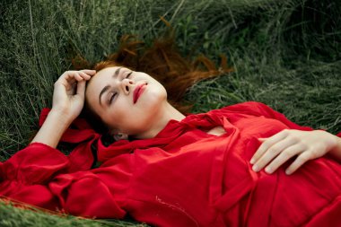 Kırmızı elbiseli güzel kadın çimen özgürlük arazisinde yatıyor.