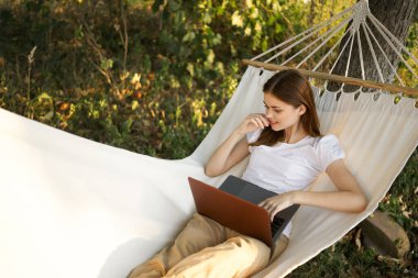 Kadınlar hamakta dizüstü bilgisayarlı tatil internetleriyle yatıyor.